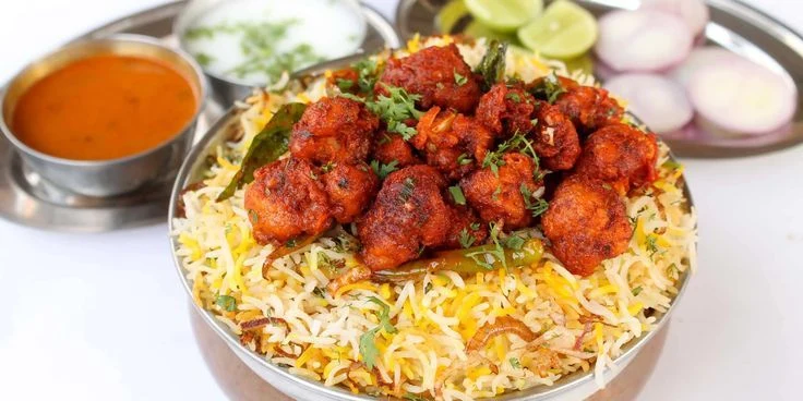 Chicken biriyani topped with fried chicken, served with curry and raita